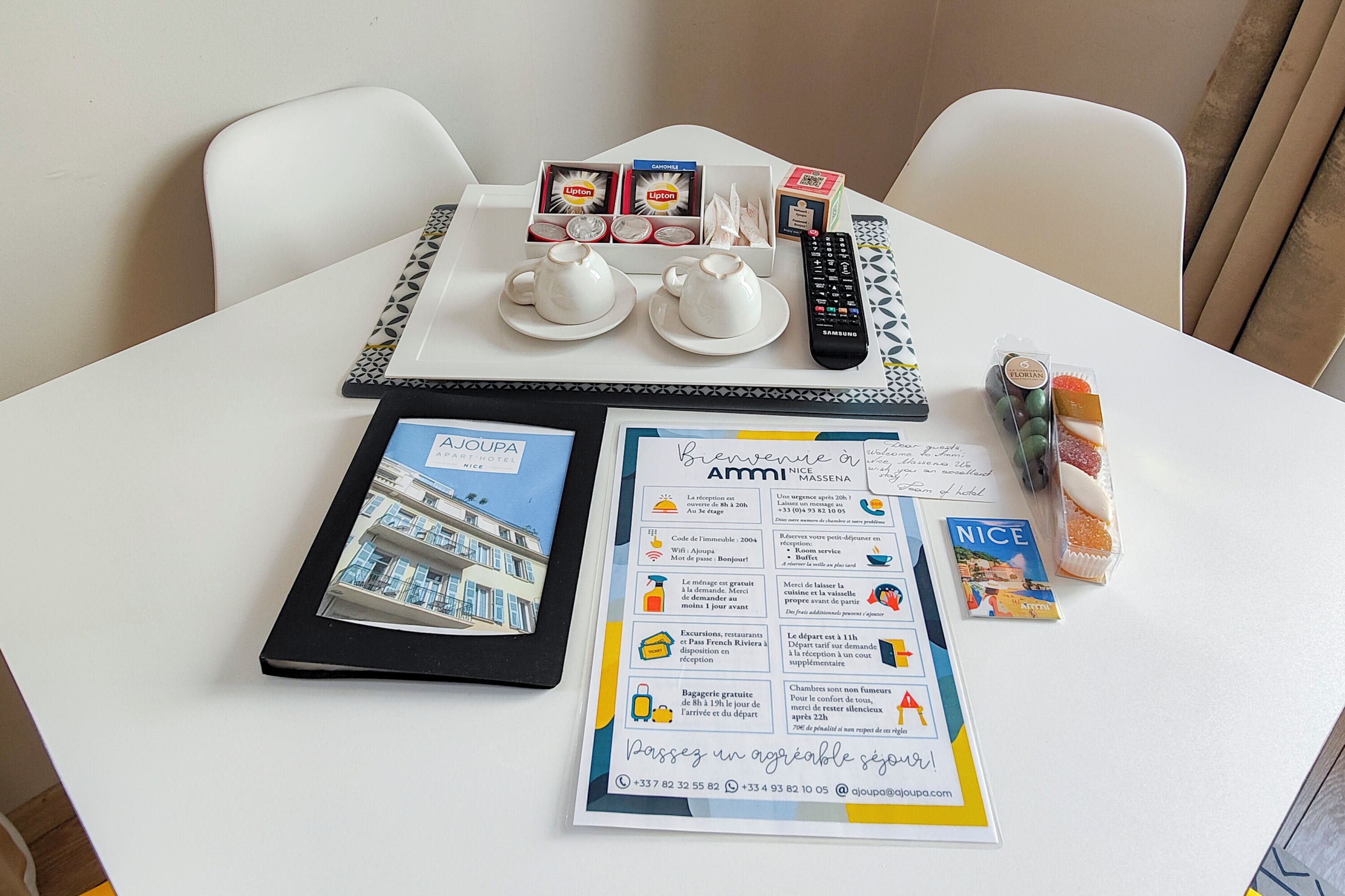 A table with a brochure, a remote control, a box of Lipton tea, a box of tissues, a small gift basket, and a framed photo.