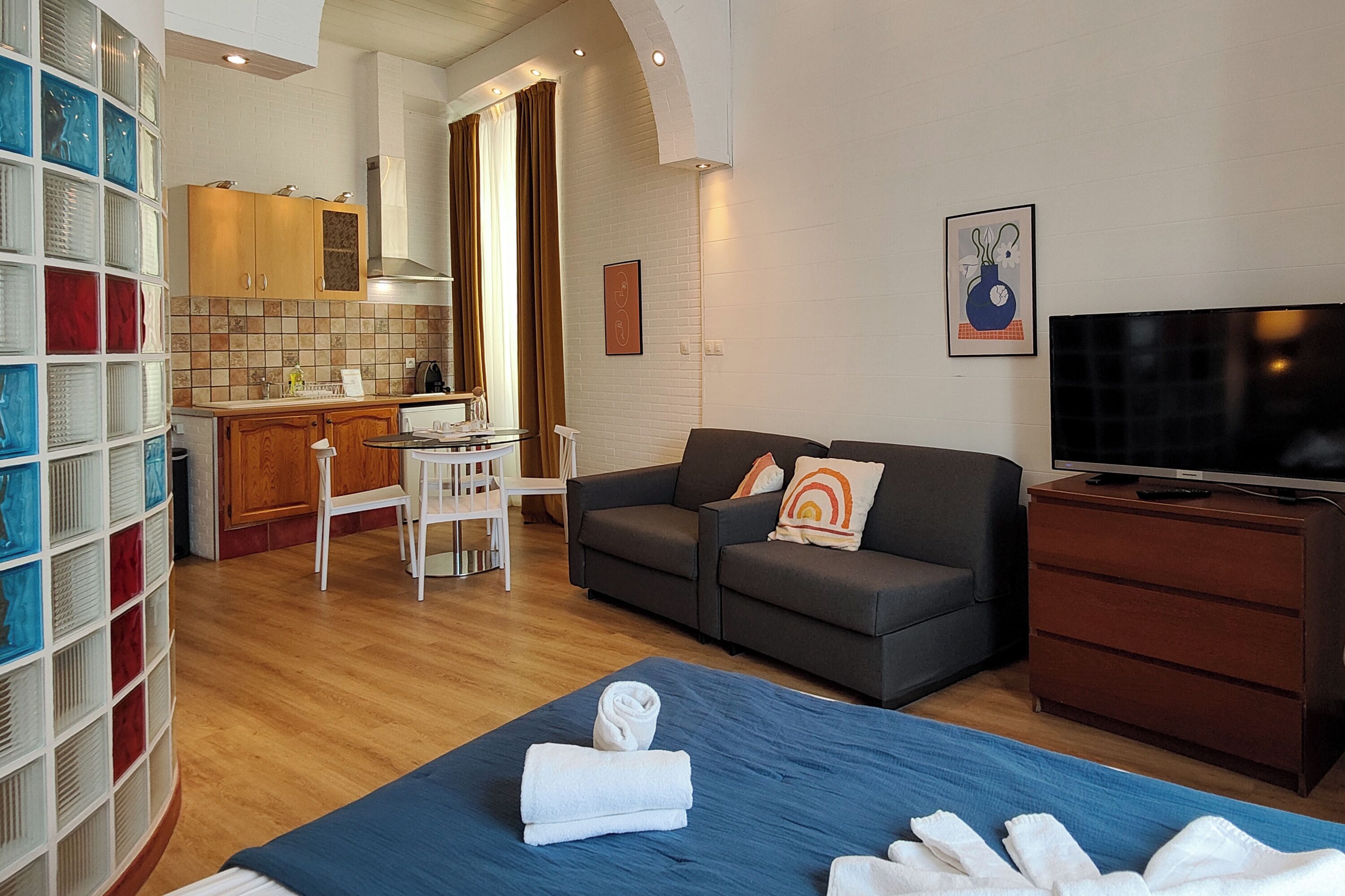 A modern living room with a sofa, a flat-screen TV, and a dining area with a kitchen in the background.