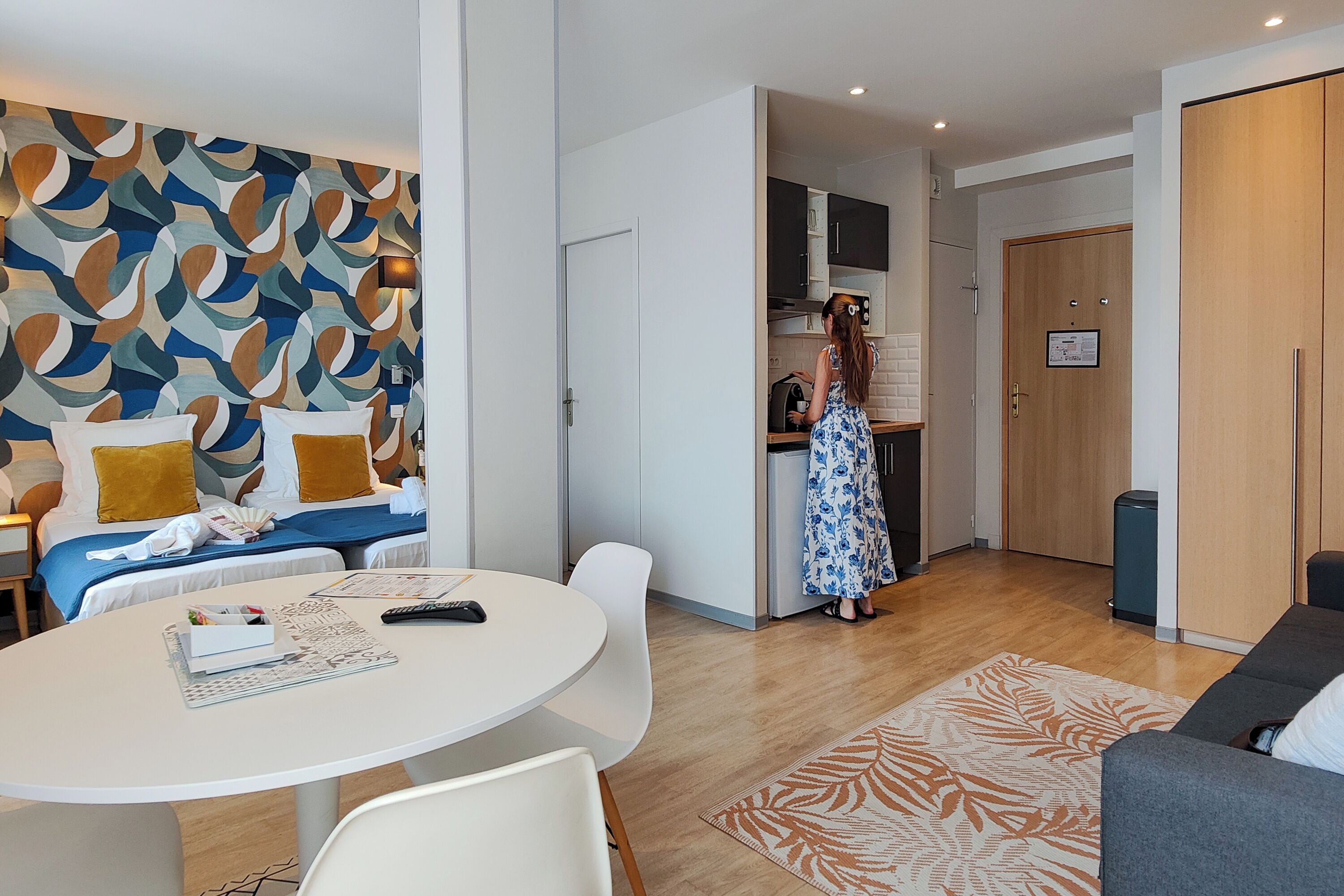 A modern hotel room with a bed, a dining table, and a kitchen area.