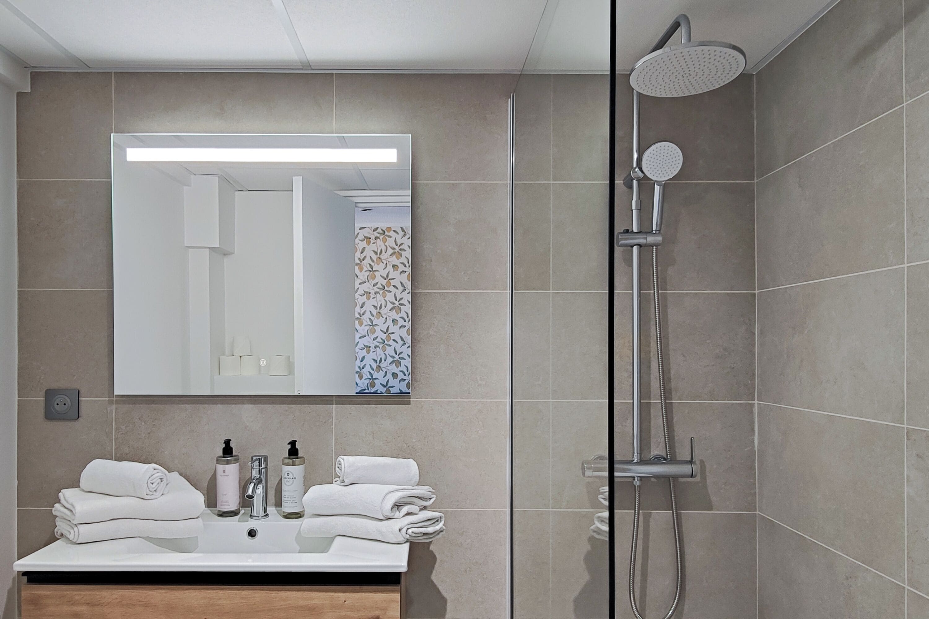 A modern bathroom with a large mirror, a sink with toiletries, and a shower.