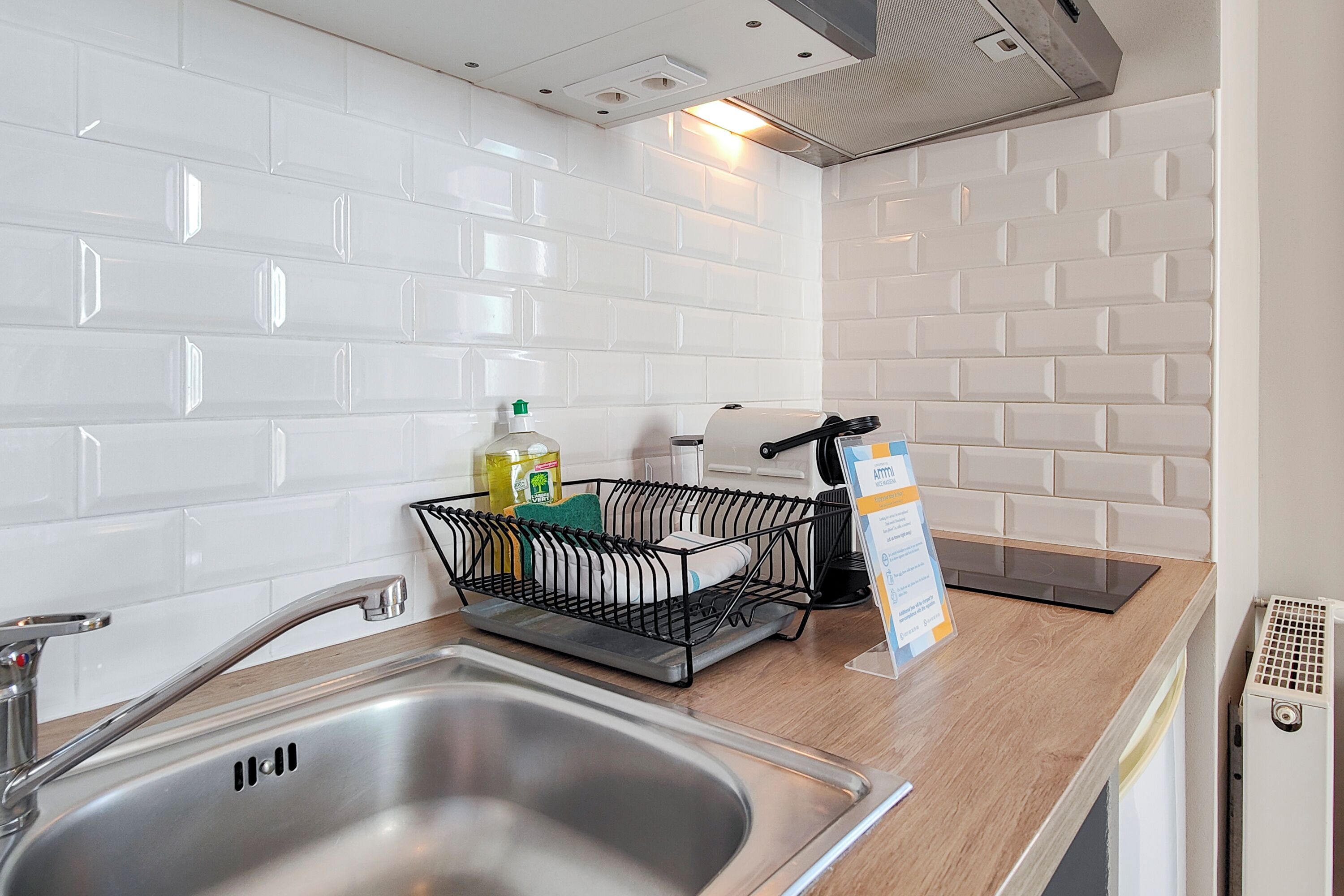 A modern kitchen with white subway tiles, stainless steel sink, and a black dish rack.
