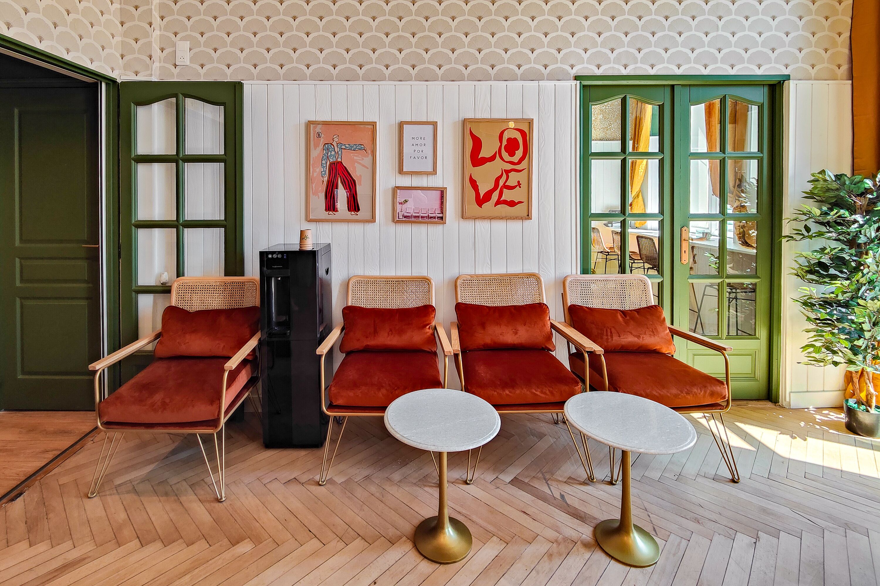 A room with four red velvet chairs, two white round tables, and a green door.