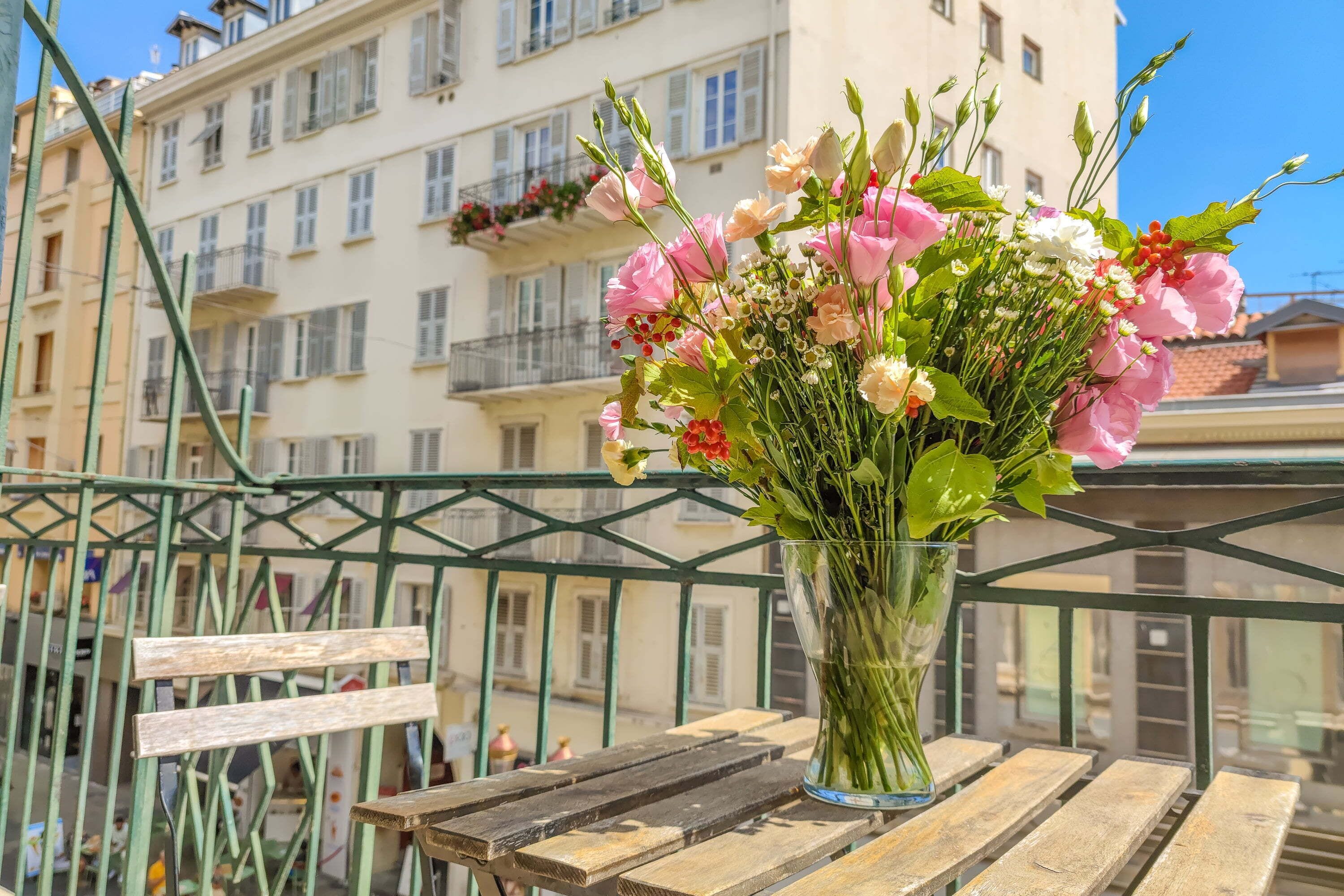 A balcony with a wooden table and a vase of flowers.