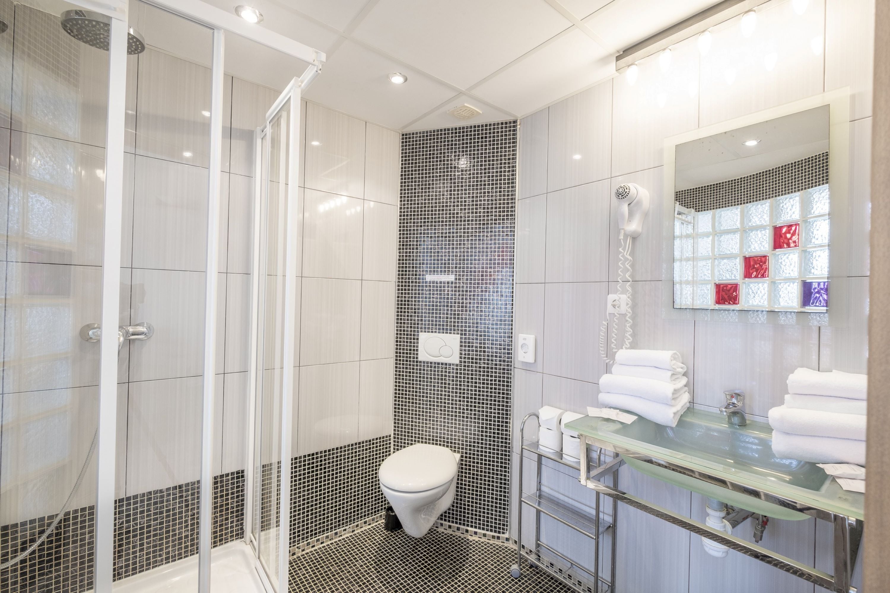 Ein modernes Badezimmer mit Duschkabine aus Glas, Toilette und Waschbecken aus Glas, inklusive Handtuchhalter.