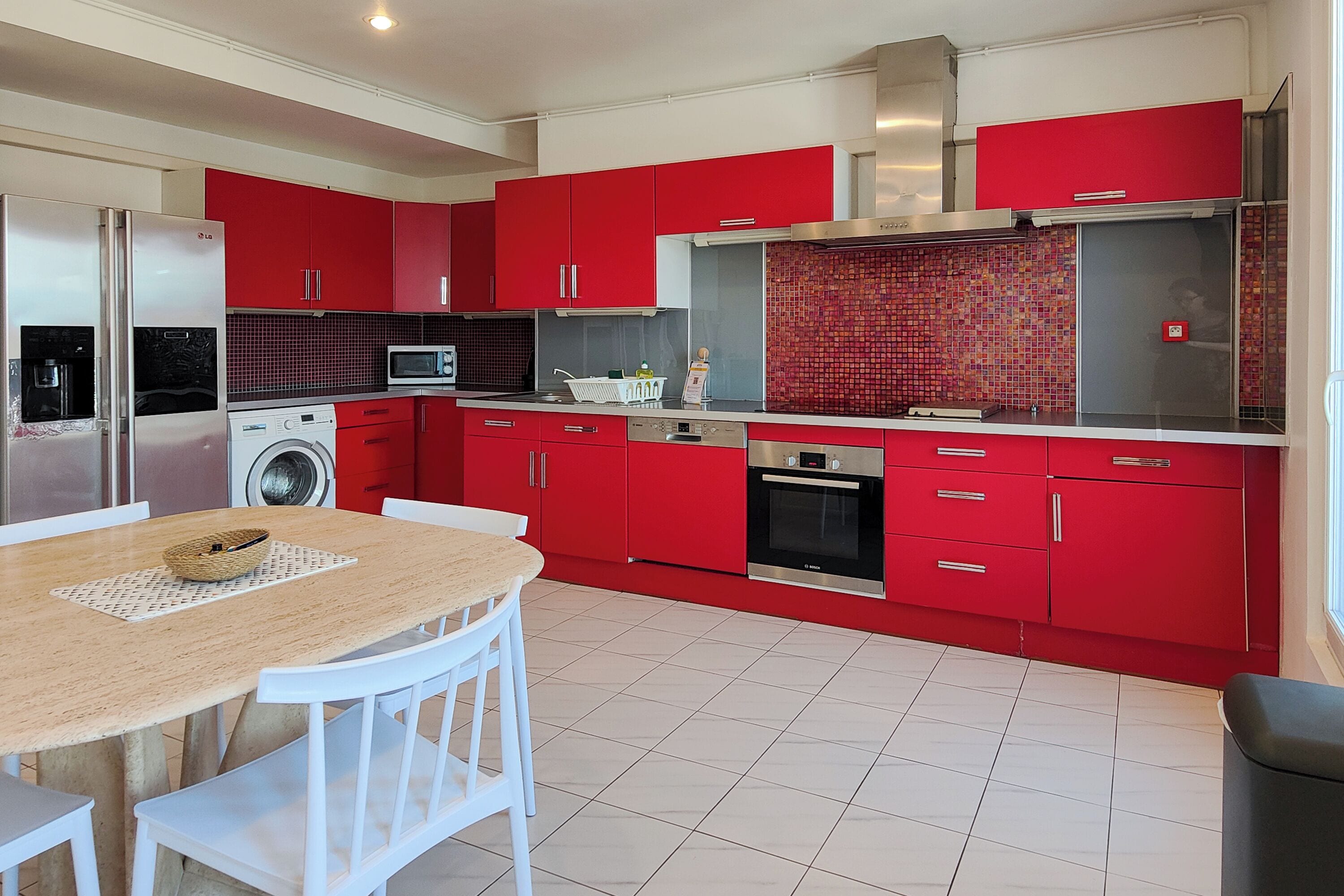Una cocina moderna con gabinetes rojos, electrodomésticos de acero inoxidable y salpicadero de azulejos.