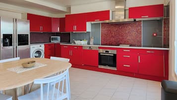 Una cocina moderna con gabinetes rojos, electrodomésticos de acero inoxidable y salpicadero de azulejos.
