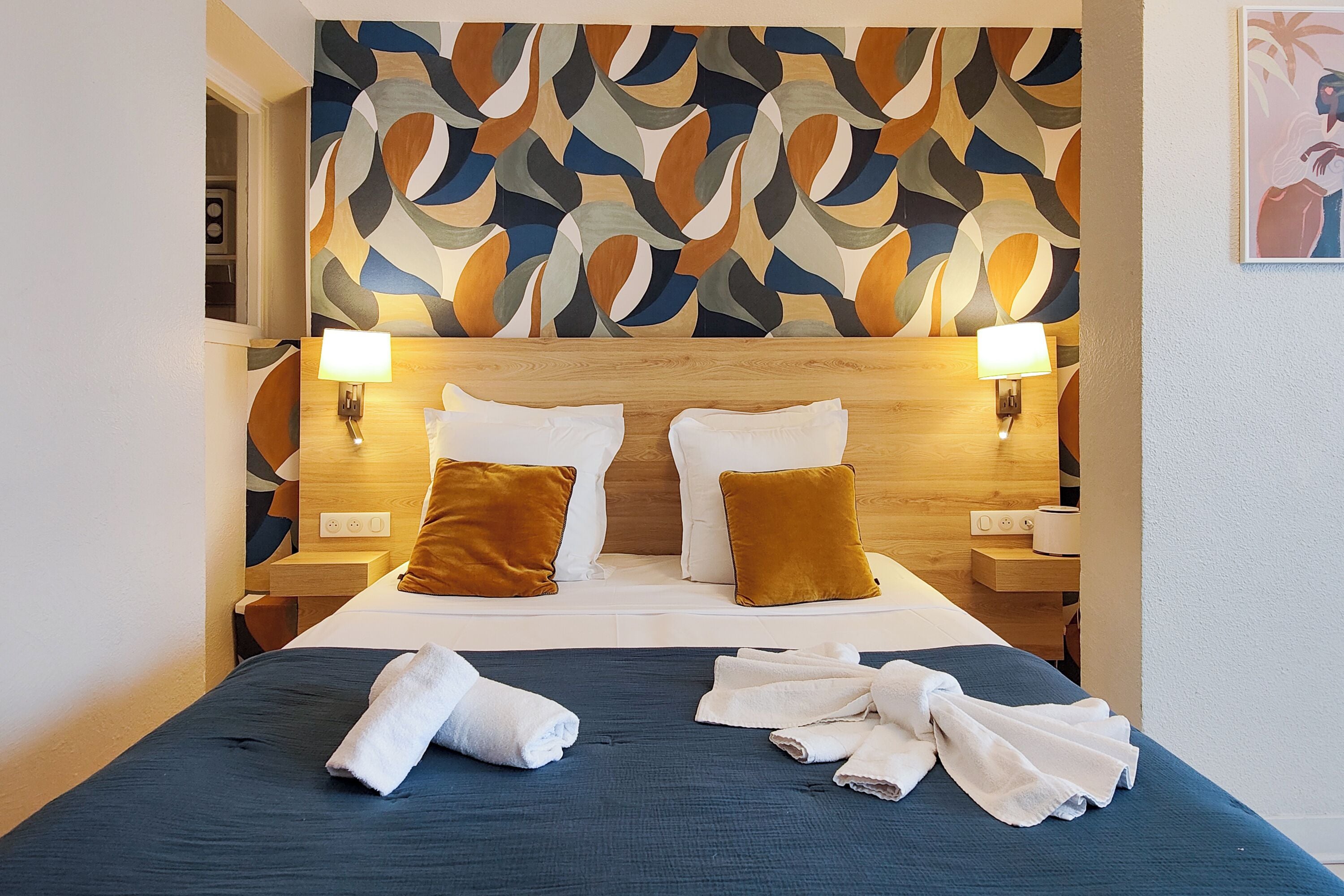 Een hotelkamer met een groot bed, twee nachtkastjes, een muur met een geometrisch patroon en een schilderij.