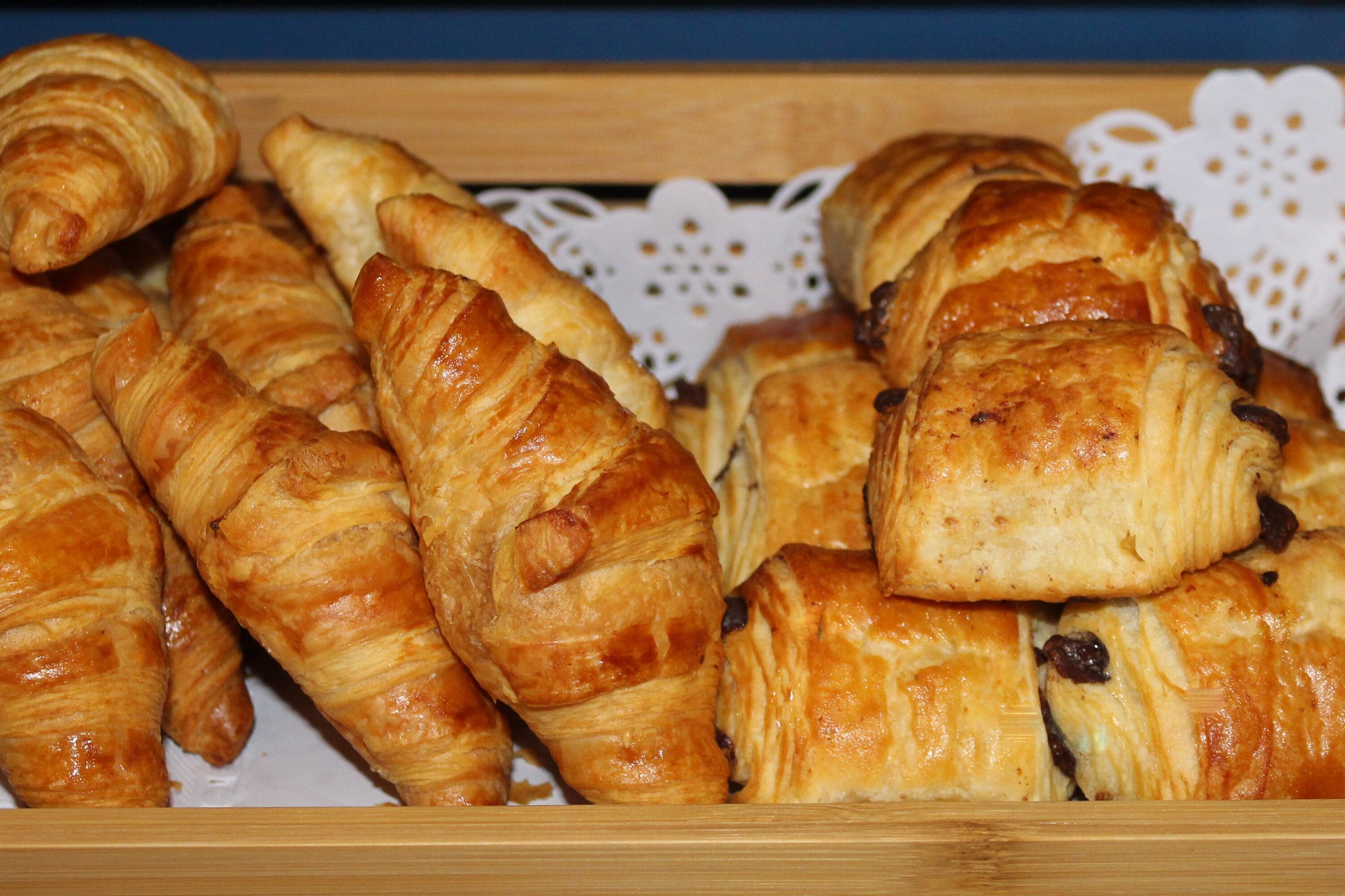 A wooden tray filled with golden-brown croissants.