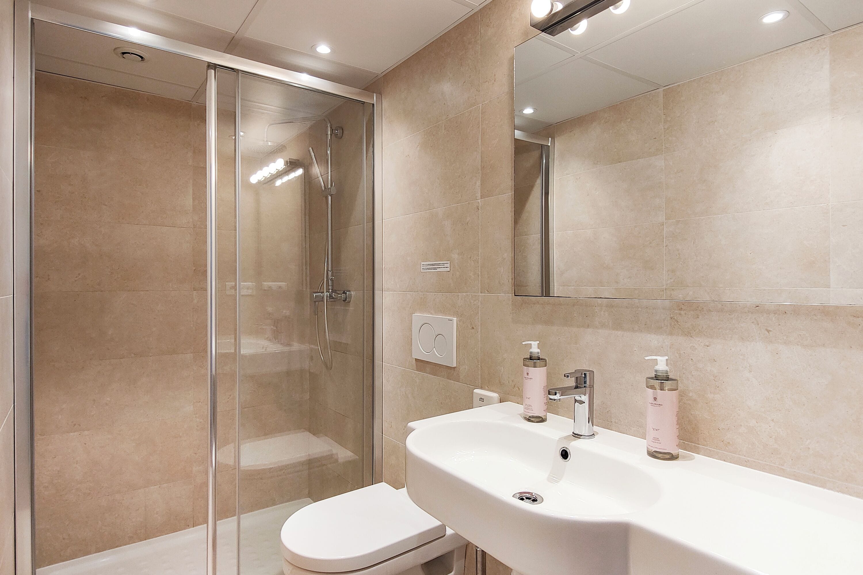 Une salle de bain moderne avec une douche à parois de verre, un lavabo blanc et un miroir.