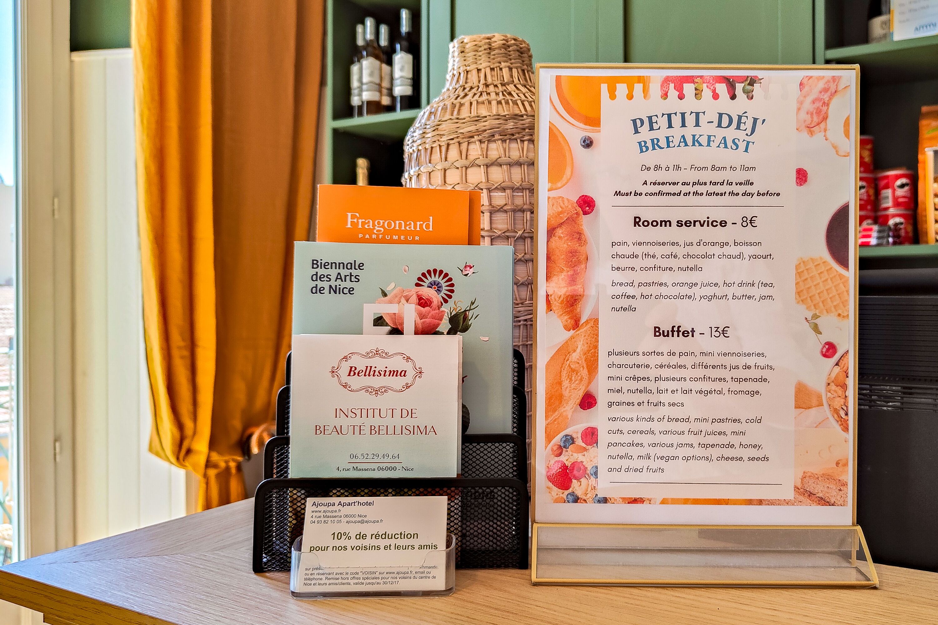 Un tableau affichant le menu du petit-déjeuner, avec les options de service en chambre et de buffet, une publicité pour un parfum et une brochure d’un institut de beauté.