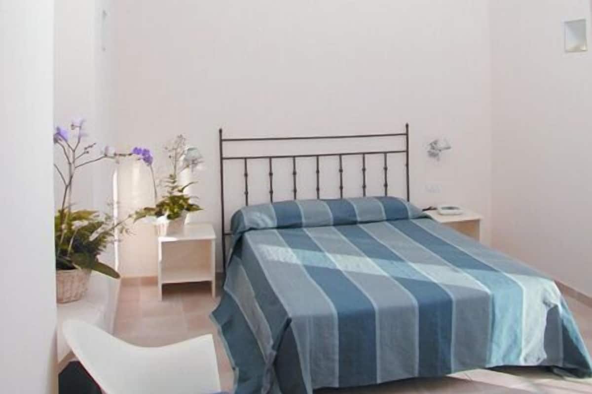 A bedroom with a bed, a chair, a nightstand, and a potted plant.