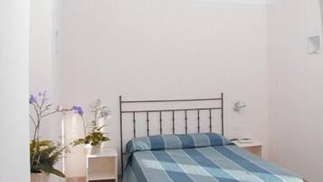 A bedroom with a bed, a chair, a nightstand, and a potted plant.