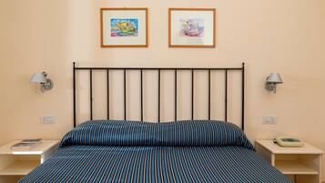 A bedroom with a bed, two bedside tables, a nightstand, a lamp, and two framed pictures on the wall.