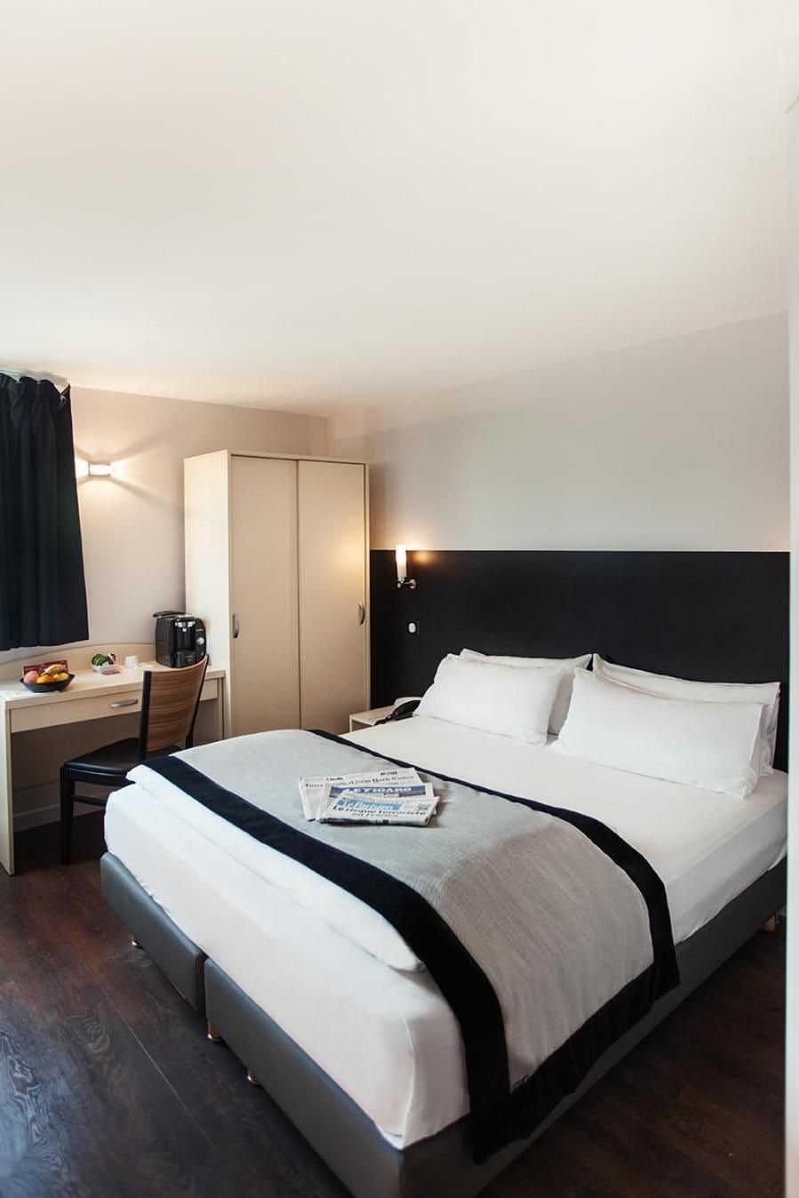 A hotel room with a bed, a desk, a chair, a wardrobe, and a nightstand.