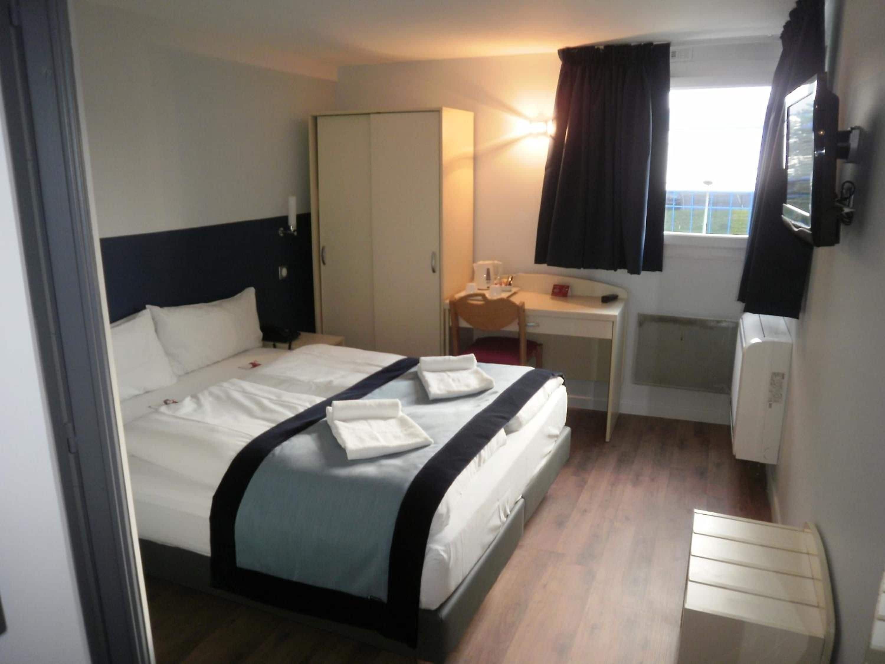 Een hotelkamer met een bed, een bureau, een stoel, een kledingkast en een raam met gordijnen.