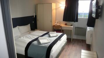 Een hotelkamer met een bed, een bureau, een stoel, een kledingkast en een raam met gordijnen.