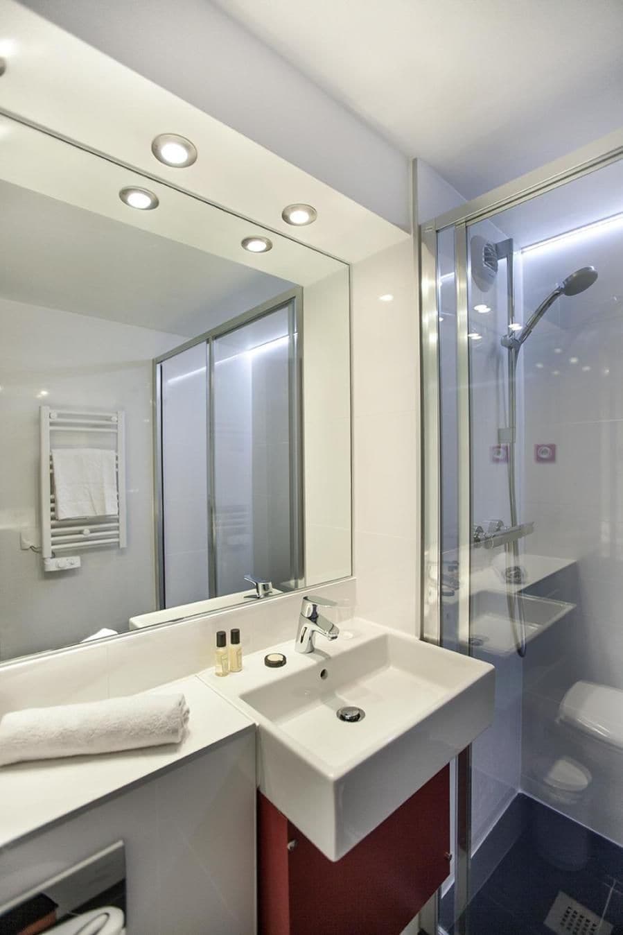 A modern bathroom with a large mirror, a white sink, and a glass-enclosed shower.