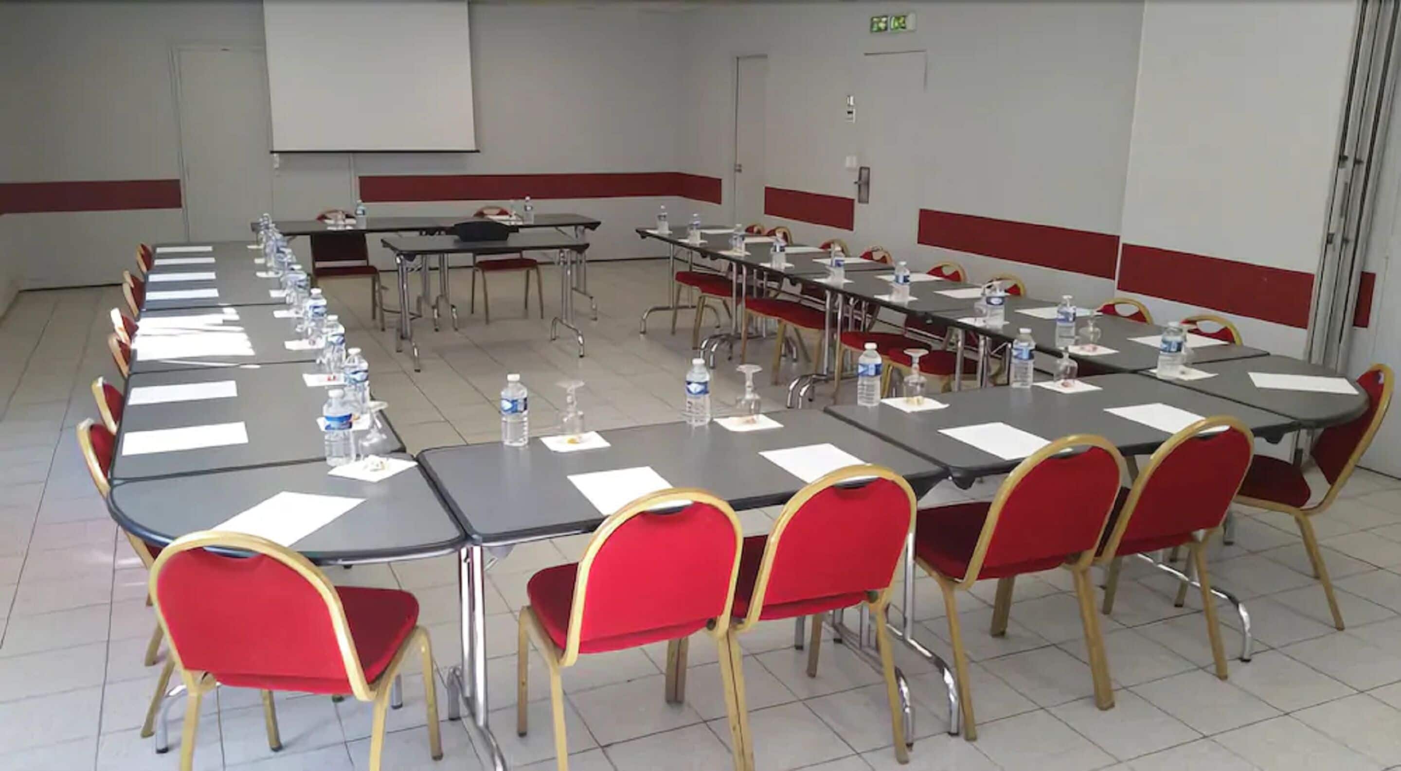 A conference room with multiple tables and red chairs, equipped with water bottles and papers.