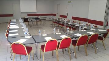 A conference room with multiple tables and red chairs, equipped with water bottles and papers.
