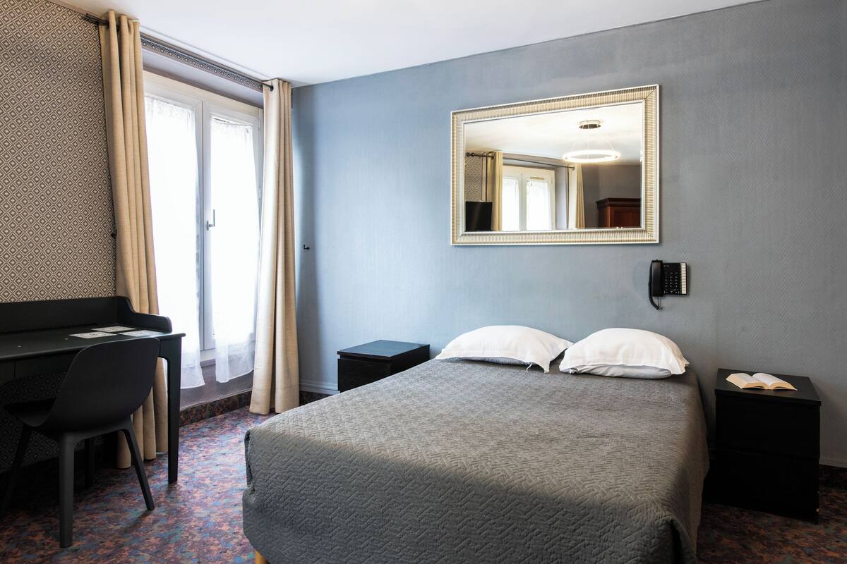 A hotel room with a bed, a desk, a chair, a nightstand, and a telephone.