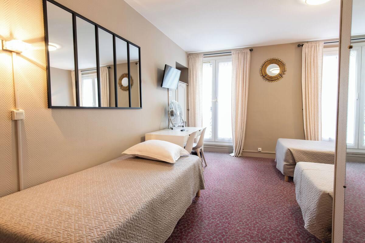 A hotel room with a bed, a desk, a chair, a TV, and a window with curtains.