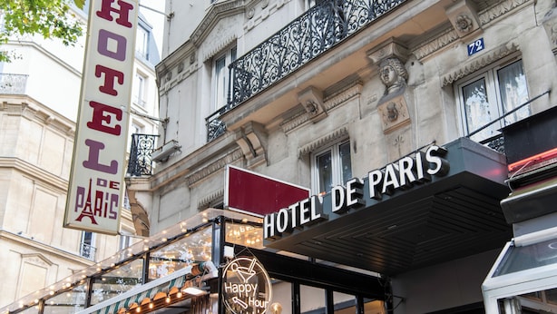 Fachada de hotel con un letrero que dice "HOTEL DE PARIS" y un letrero de neón que indica "Happy Hour".