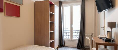 Una habitación de hotel con cama, escritorio con silla, televisor y armario.