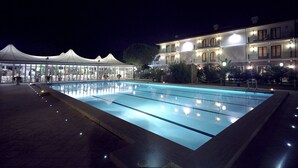 A swimming pool with a tiled deck, adjacent to a building with multiple balconies and a covered outdoor area with seating. - Park Hotel Villa Ariston (Camaiore)
