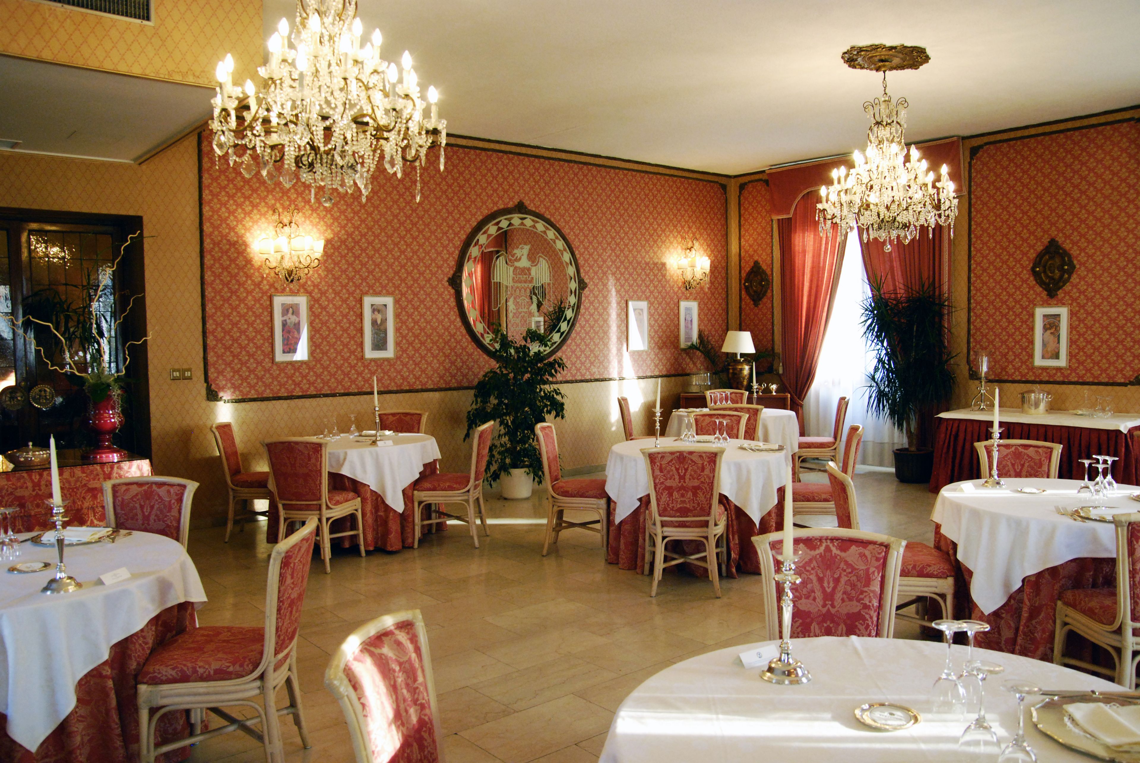 Un comedor con mesas dispuestas para el servicio, sillas tapizadas en rojo y candelabros.