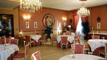 Un comedor con mesas dispuestas para el servicio, sillas tapizadas en rojo y candelabros.