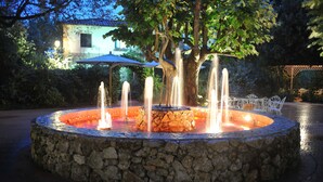 A stone fountain with water jets, surrounded by a paved area and trees. - Park Hotel Villa Ariston (Camaiore)