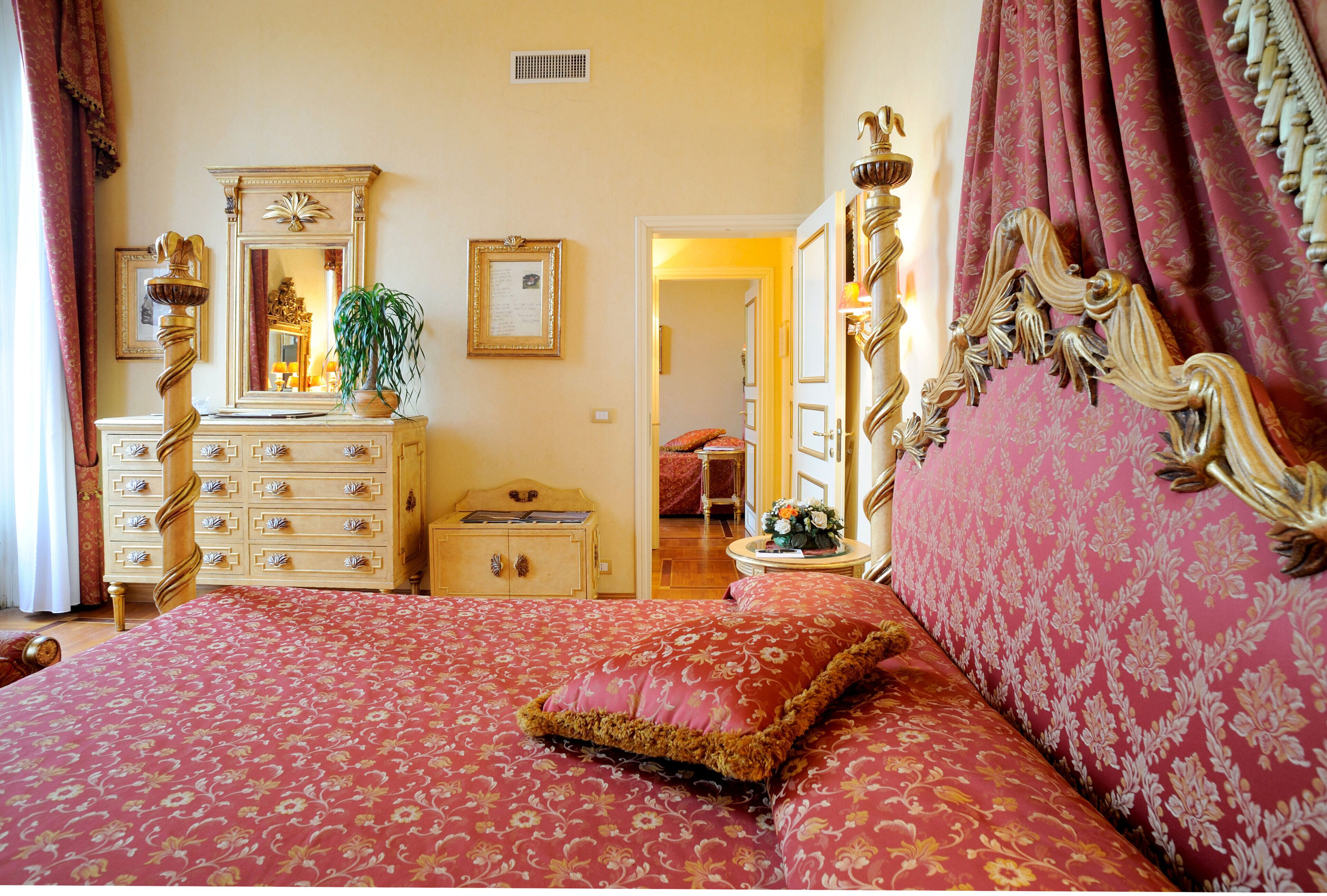 A bedroom with a large bed, a dresser, a mirror, and a door leading to another room.