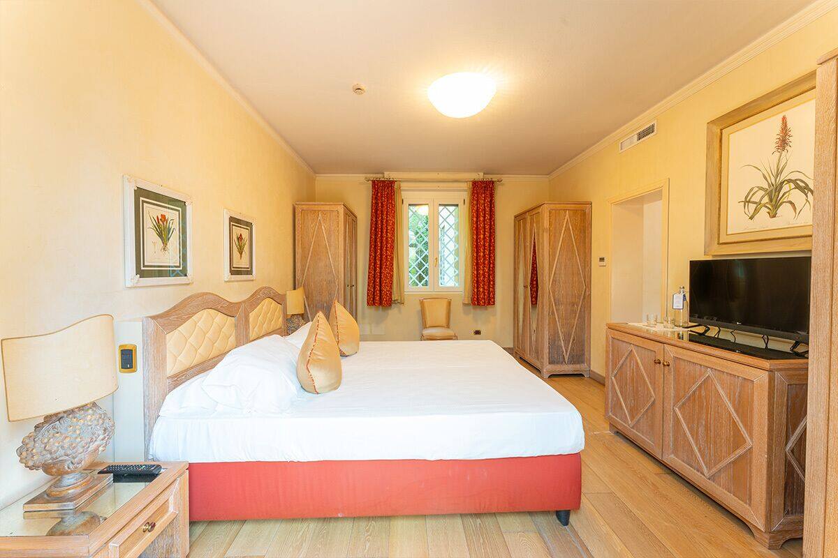 Ein Schlafzimmer mit einem großen Bett, einem Fernseher, Holzmöbeln und gerahmten Pflanzenbildern an den Wänden.