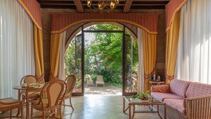 A spacious room with a wooden floor, a dining area with wicker furniture, a sofa, and a glass coffee table. - Park Hotel Villa Ariston (Camaiore)
