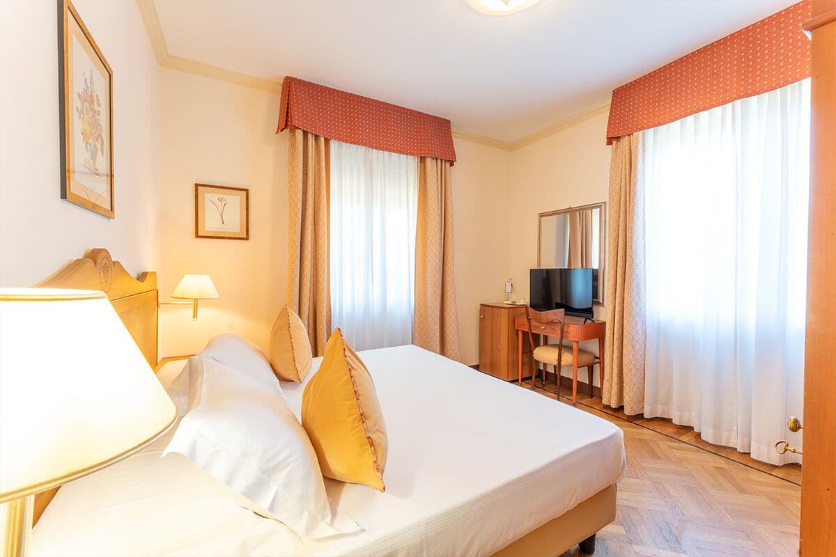 Ein Hotelzimmer mit Bett, Schreibtisch und Fernseher, sowie Vorhängen.