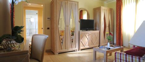 Ein Hotelzimmer mit einem Holzschrank, einem Fernseher, einem Sofa, einem Sessel und einem Couchtisch.