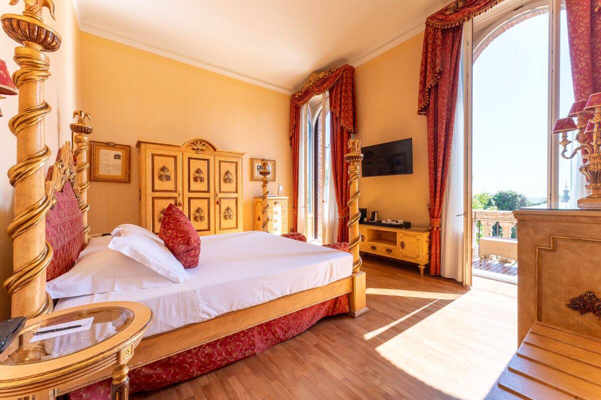 Ein Schlafzimmer mit einem großen Bett, einem Holz-Kopfteil, einem Nachttisch, einem Fernseher und einem Balkon mit Aussicht.