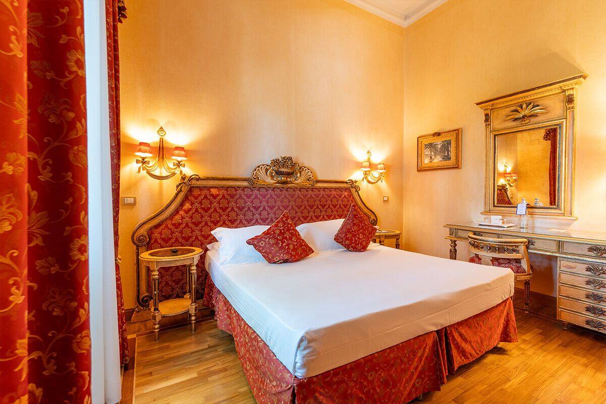 Ein Hotelzimmer mit einem großen Bett, einem Schminktischchen, einem Frisierbildschirm und zwei Wandleuchten.