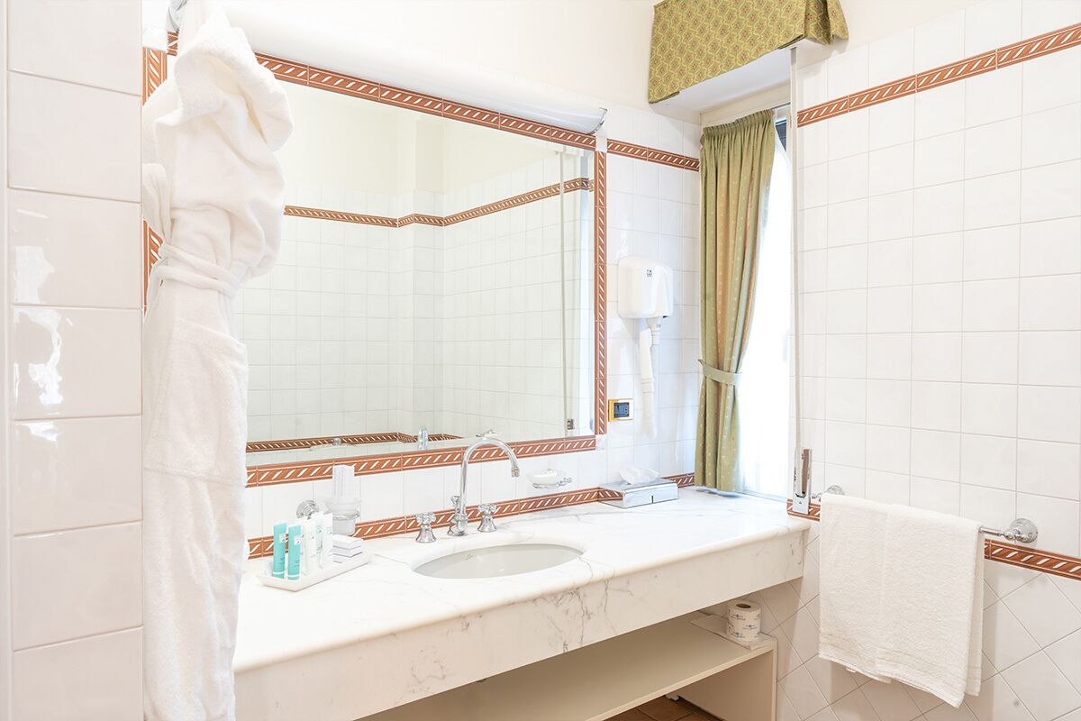 Un baño con lavamanos blanco, espejo y toallero.