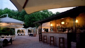 An outdoor patio area with brick flooring, white umbrellas, and a bar with stools. - Park Hotel Villa Ariston (Camaiore)