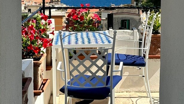 Una terraza con una mesa y sillas, vista al mar y un edificio con un campanario en el fondo.