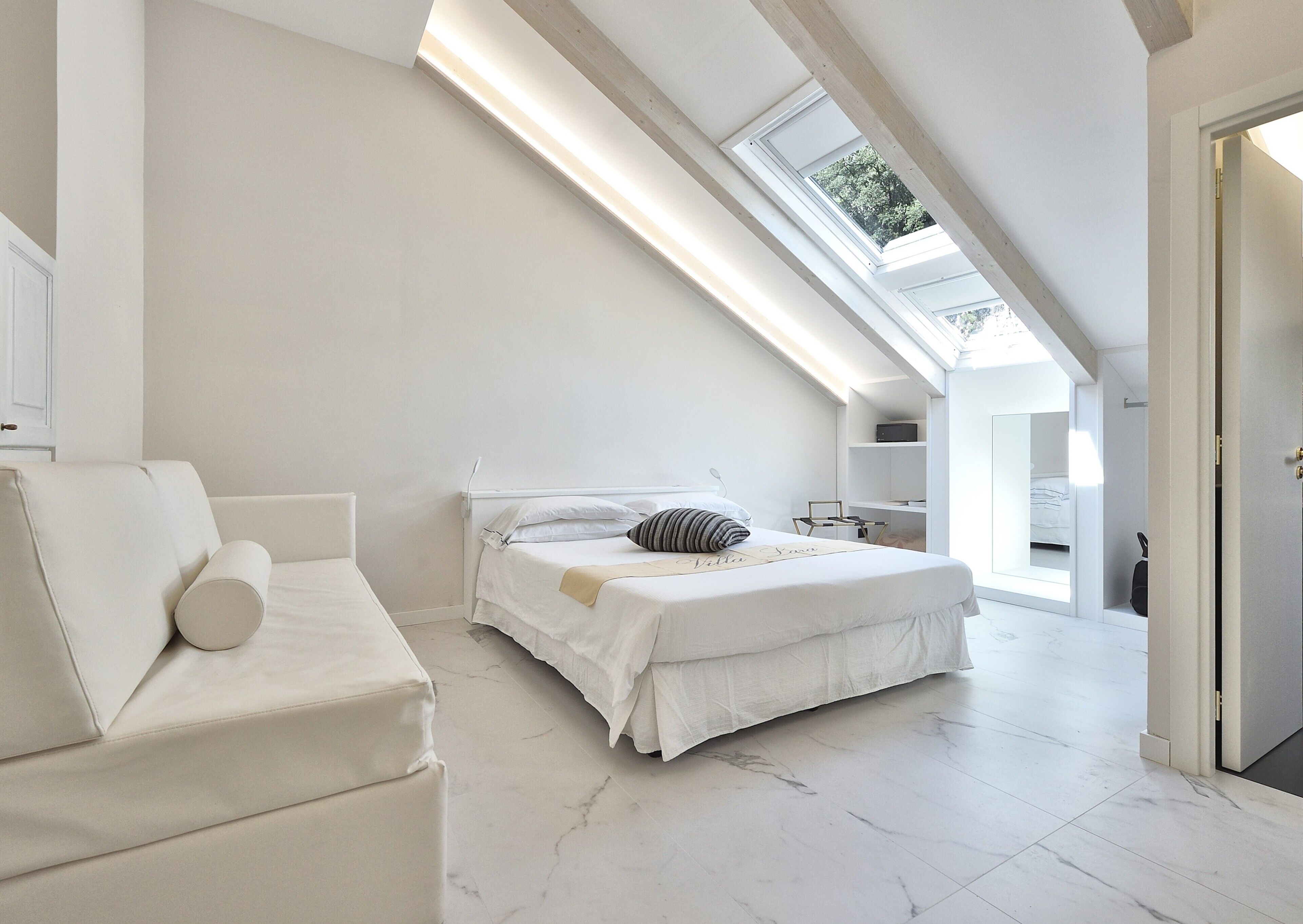 A modern bedroom with a skylight, a bed, a sofa, and a walk-in closet.