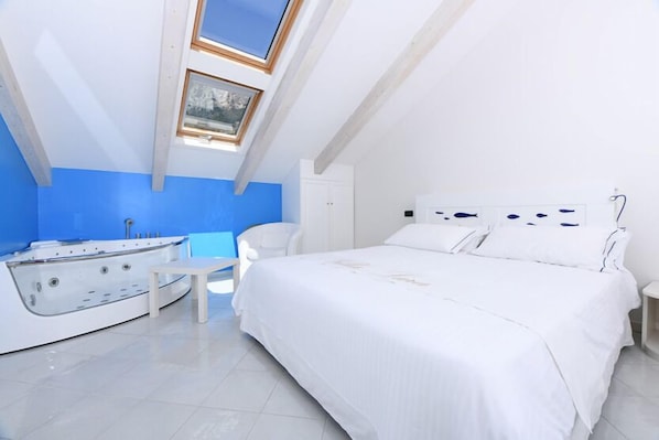 Un dormitorio con una cama grande, una mesita pequeña, una silla y una bañera con forma de barco.