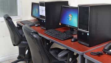 A row of four desktop computers on a desk with two black office chairs.