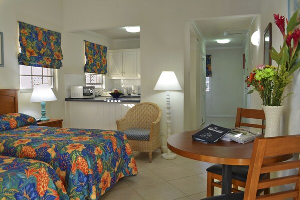 A hotel room with a bed, a dining table, a chair, a small kitchen area, and a bathroom visible through an open door. - Blue Orchids Beach Hotel (Worthing)