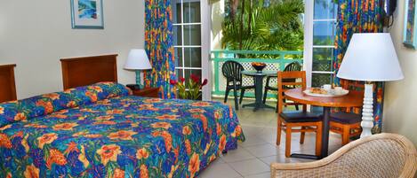 A hotel room with a bed, a chair, a table, and a balcony with a view of greenery.