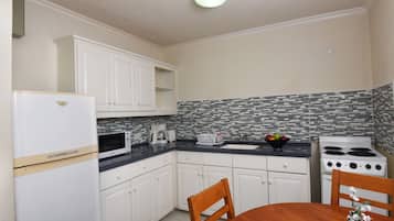 A compact kitchen with white cabinets, a microwave, a toaster, a sink, and a stove.