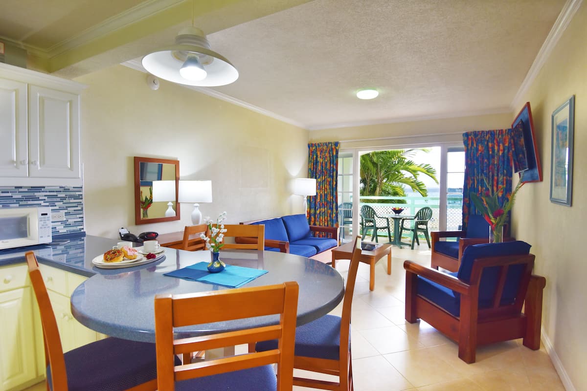 A dining area with a round table, chairs, and a blue sofa. There is a kitchen area with a microwave and cabinets.