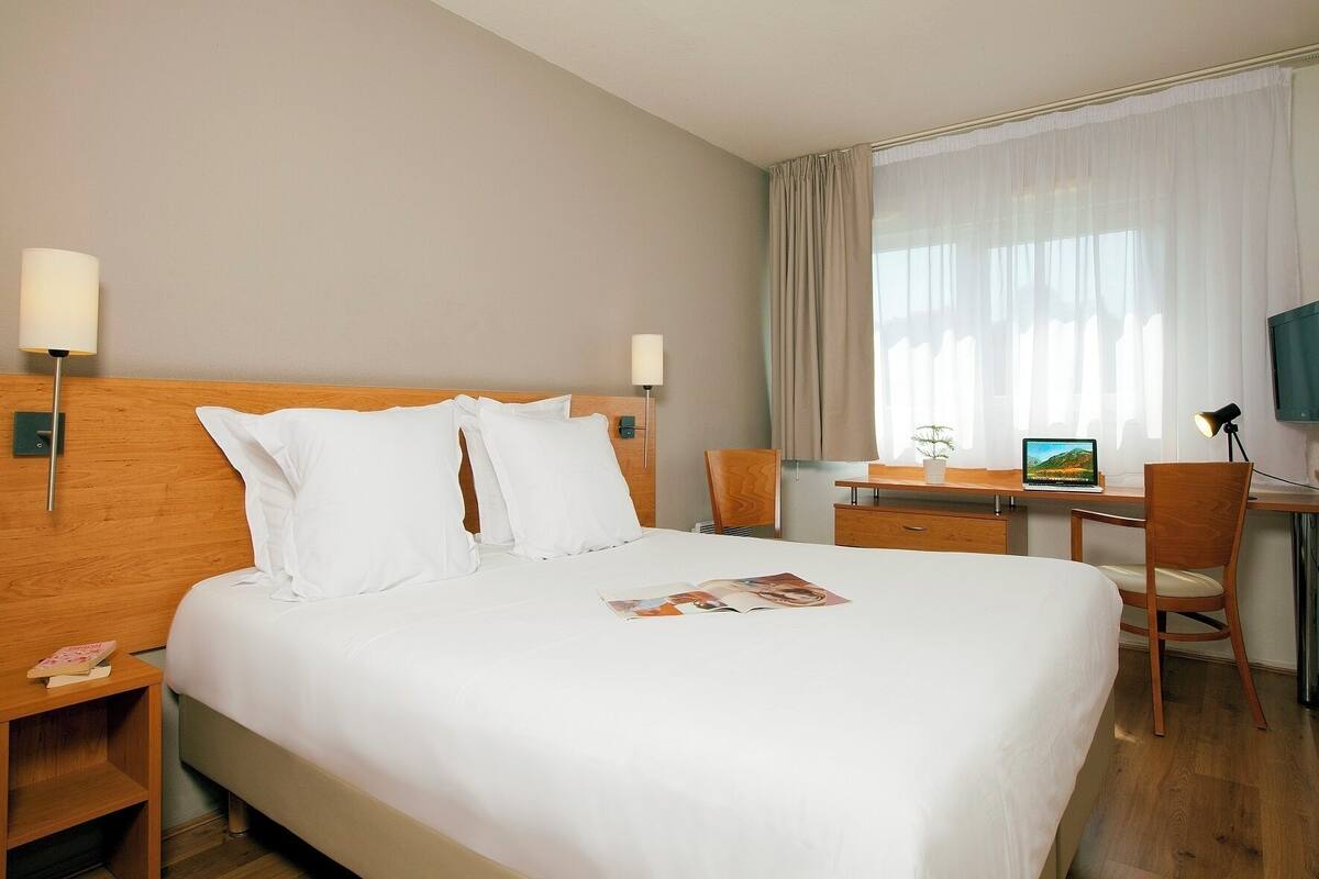 Una habitación de hotel con cama, escritorio, silla, lámpara y televisión.