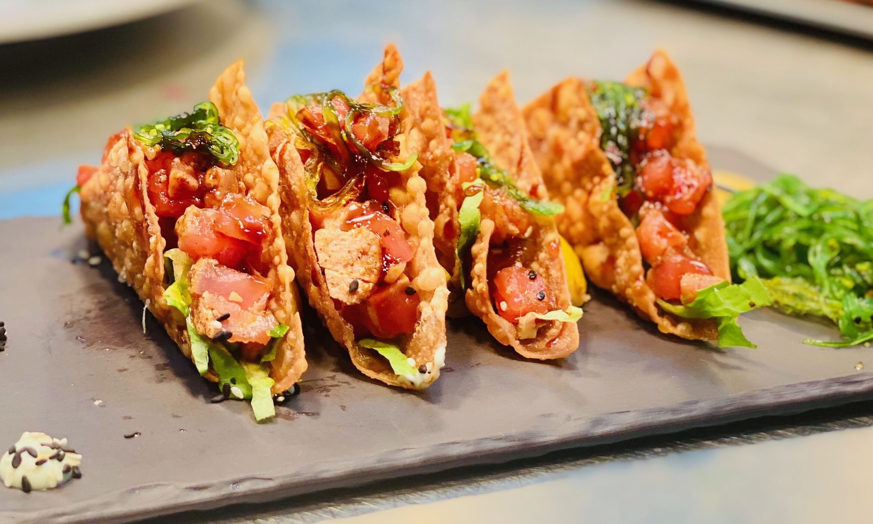 A plate of food with tacos filled with lettuce, tomatoes, and possibly cheese, served on a dark slate plate.